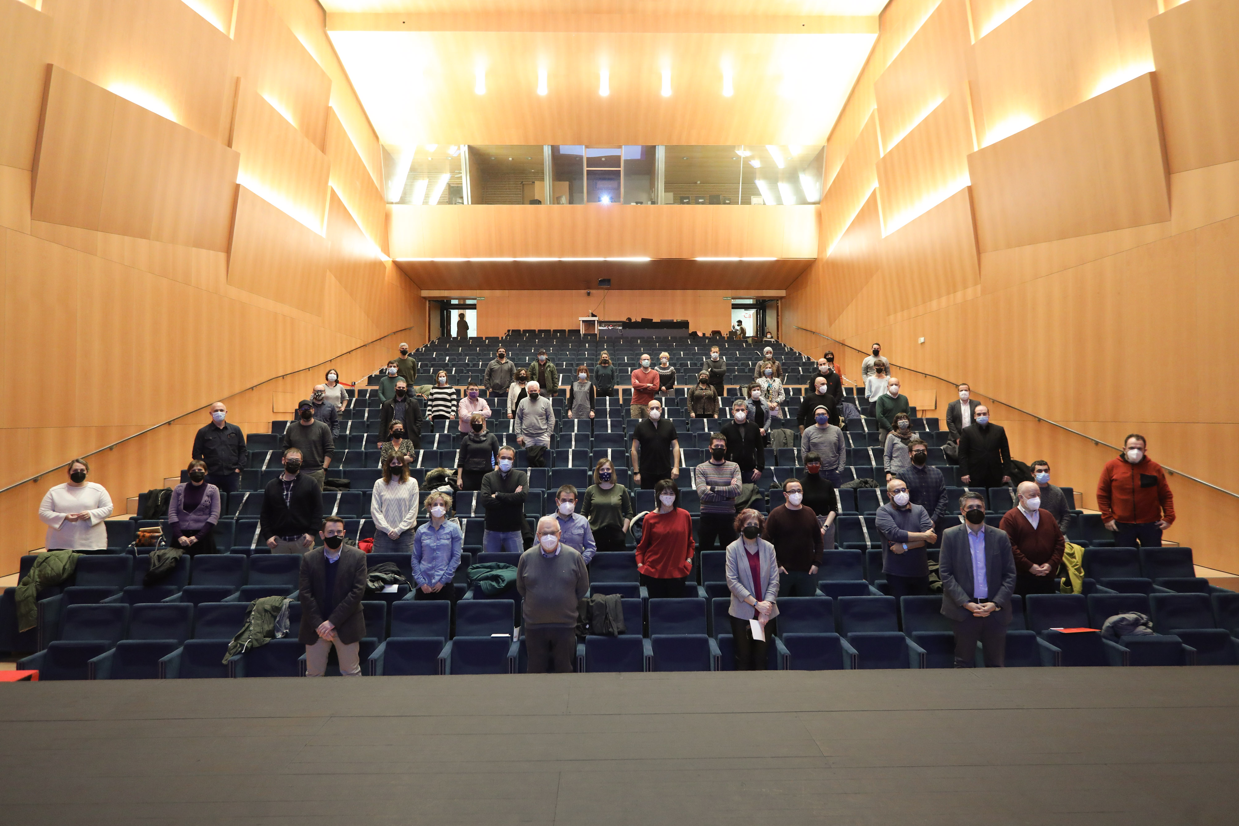 Fotografía de una sala con butacas y con personas que están de pie.