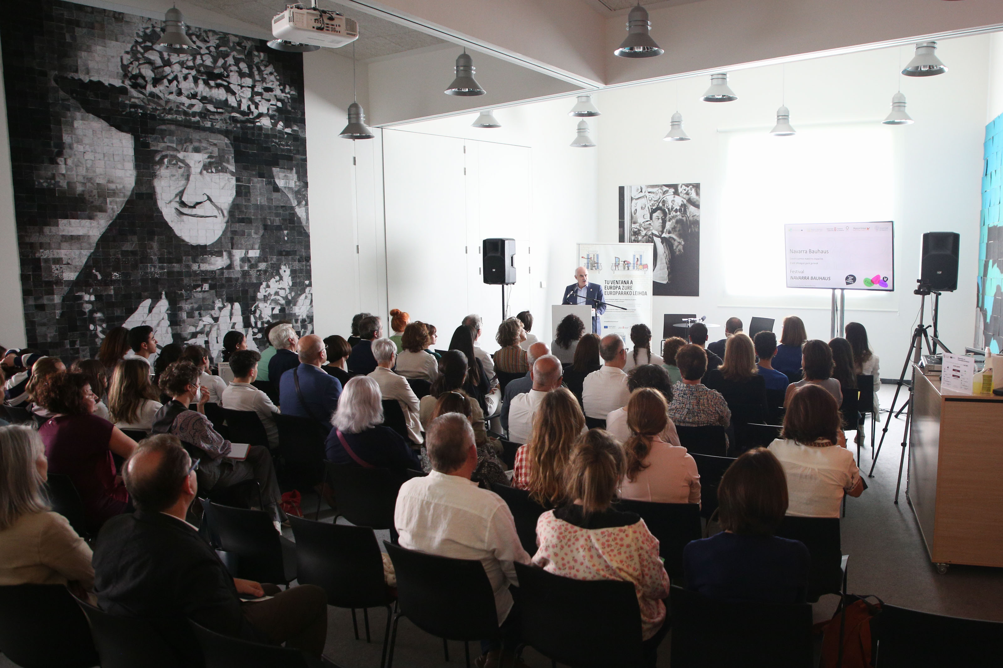 Fotografía de la presentación del festival, en la que aparecen muchas personas sentadas y en el atril el vicepresidente hablando de pie