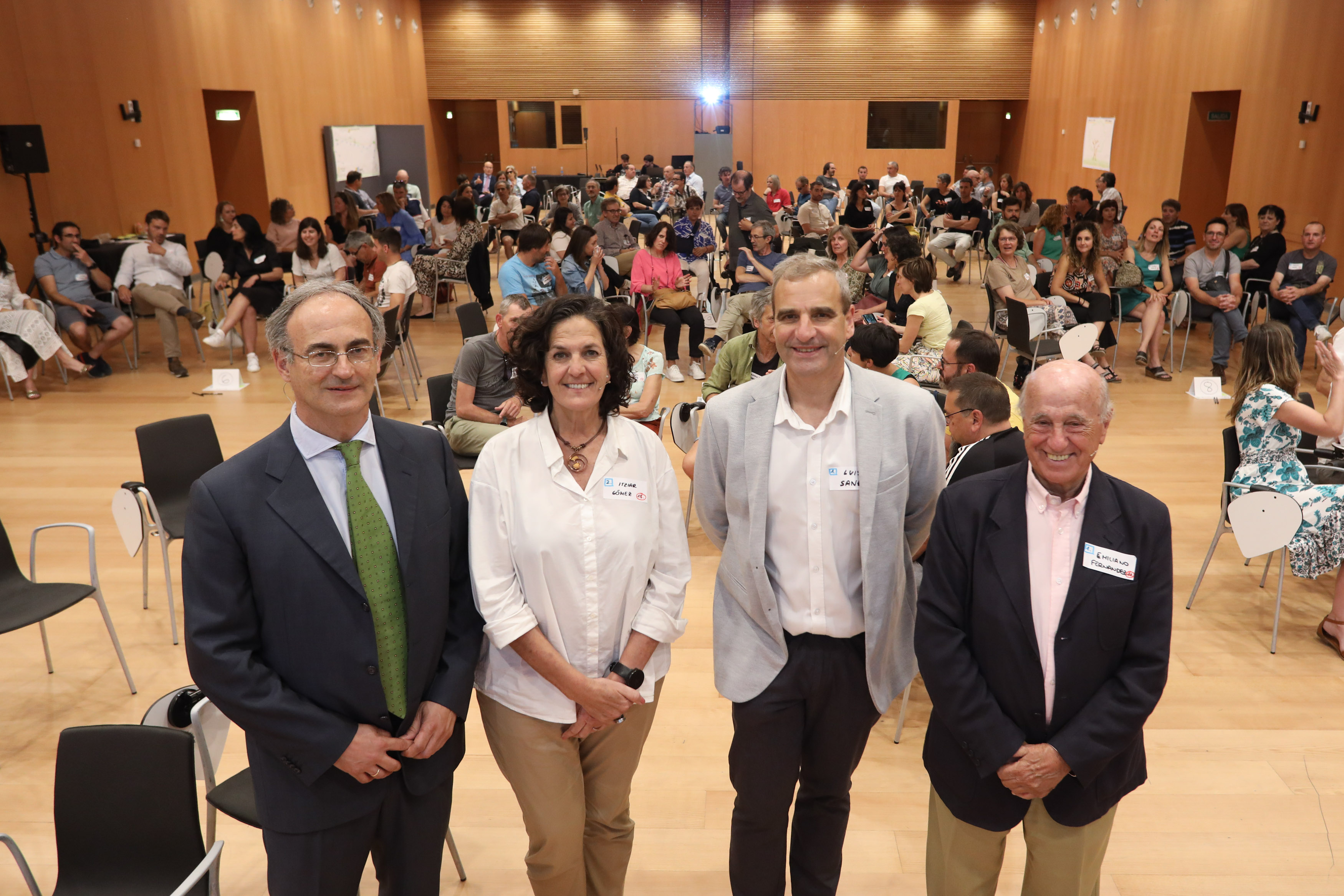 Fotografía de cuatro personas de pie dentro de una sala y otras sentadas.