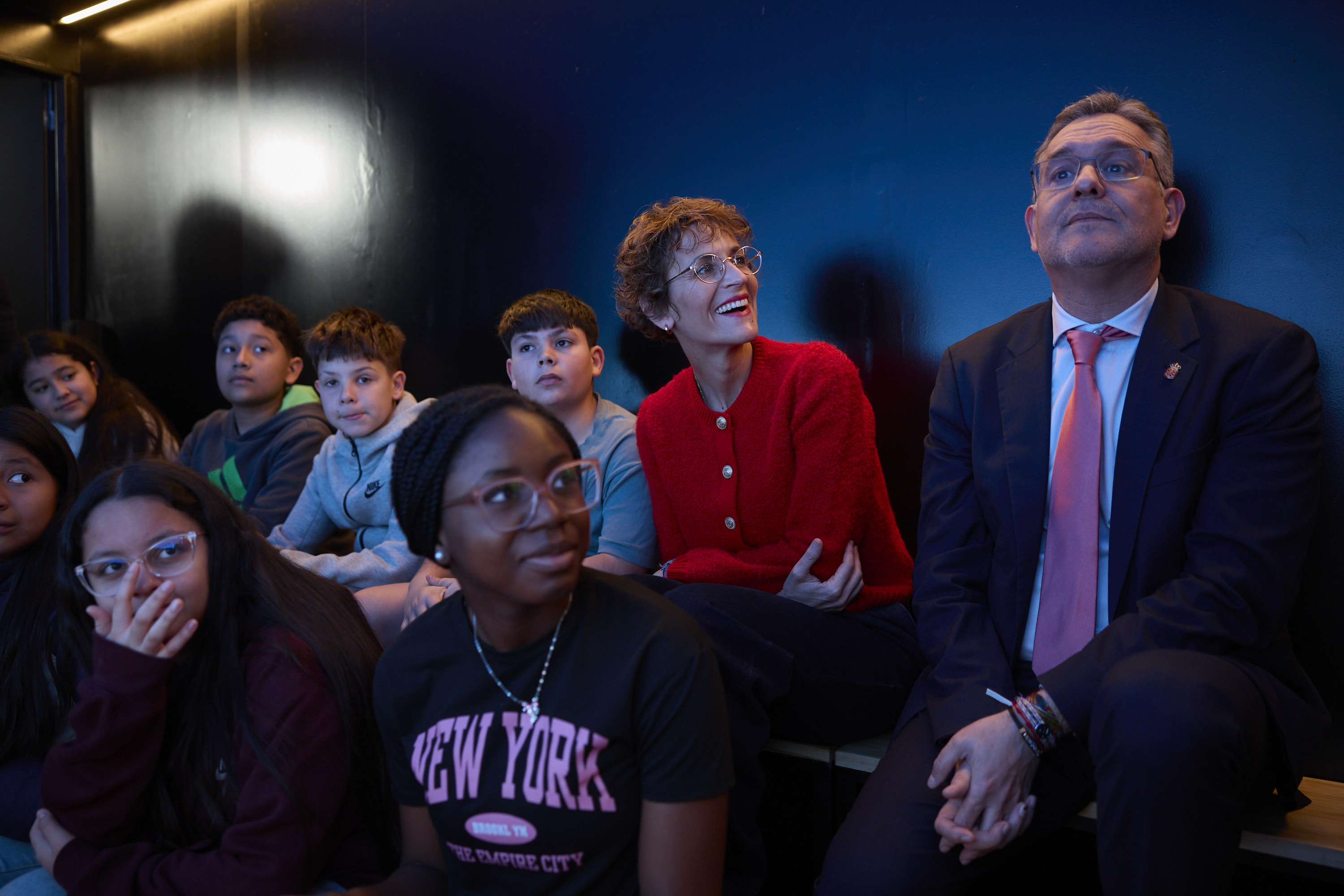 Imagen en la que se aprecia un grupo de niños con dos personas adultas sentados