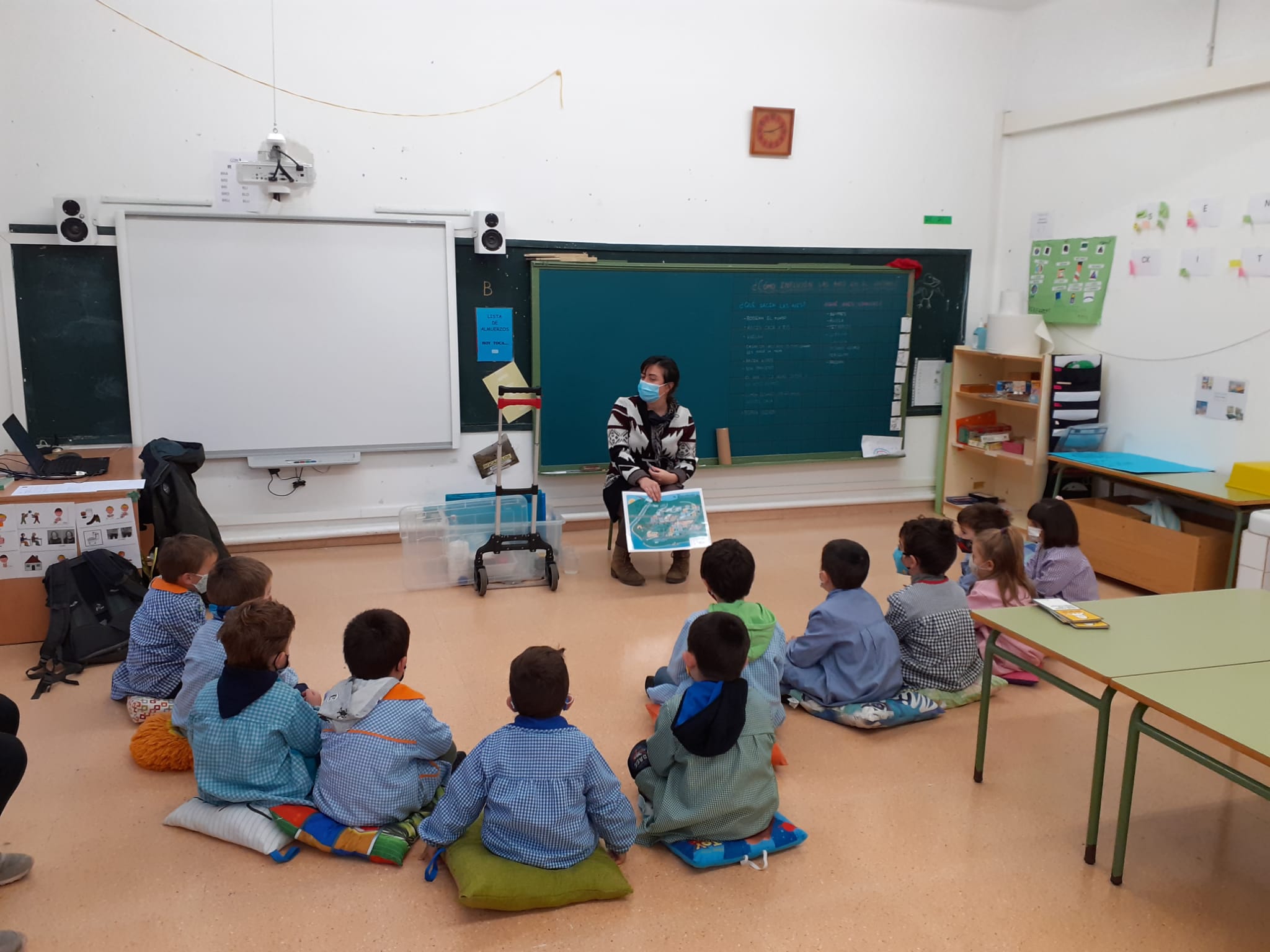 Fotografía de doce niños sentados en el suelo en un aula y una persona trabajadora de Nilsa