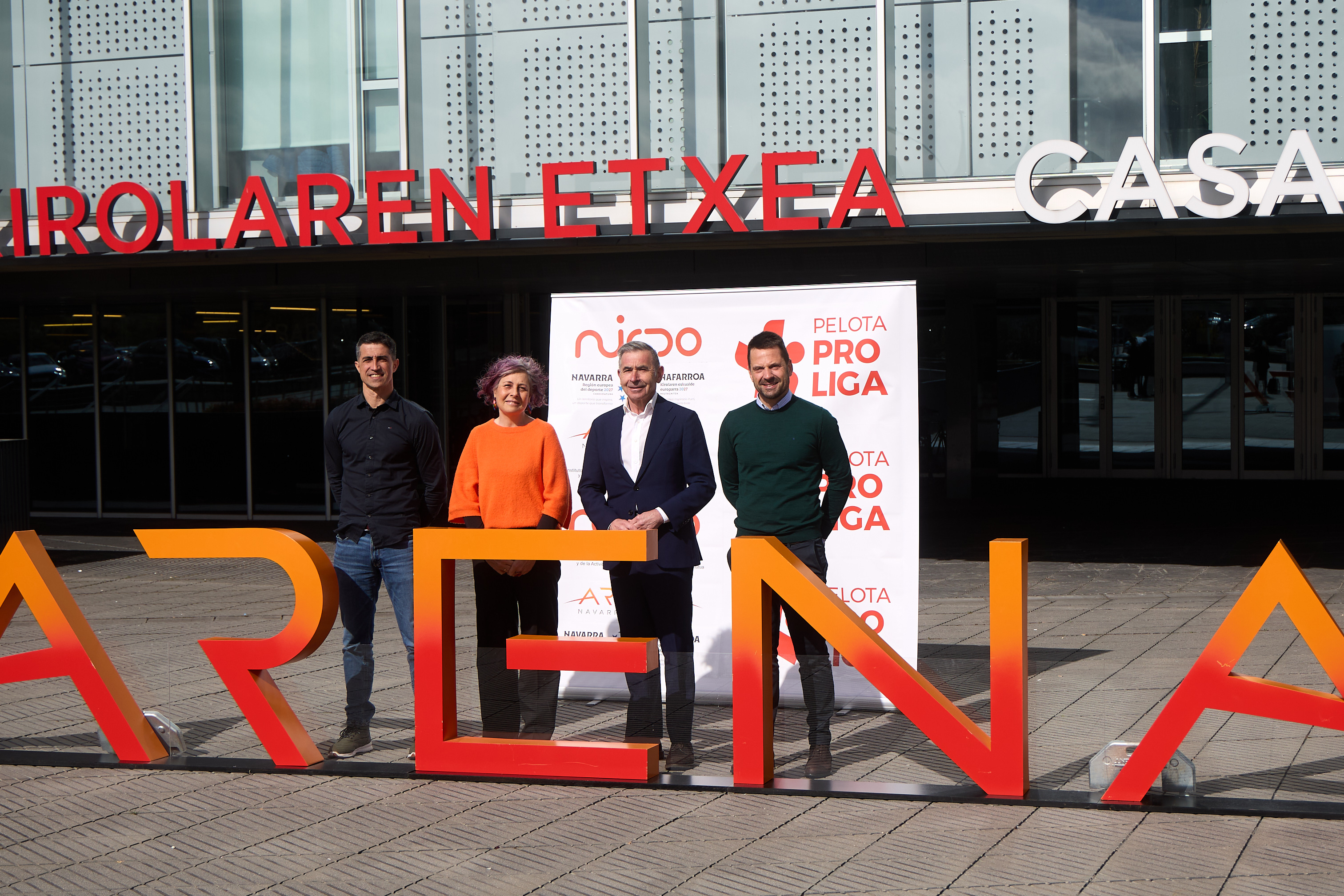 Cuatro personas posando delante del Navarra Arena con los logos