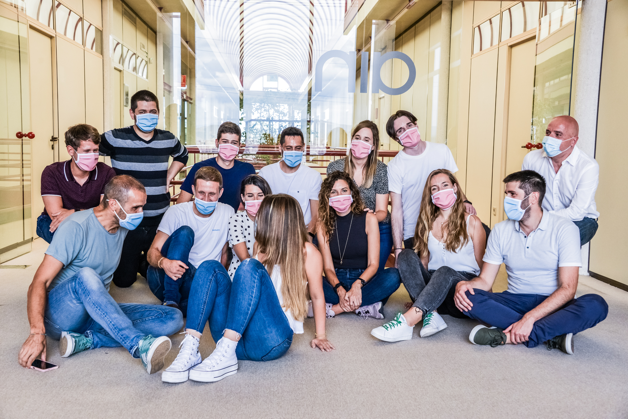 Fotografía de interior donde aparece un grupo de mujeres y hombres con mascarilla sentados en el suelo.