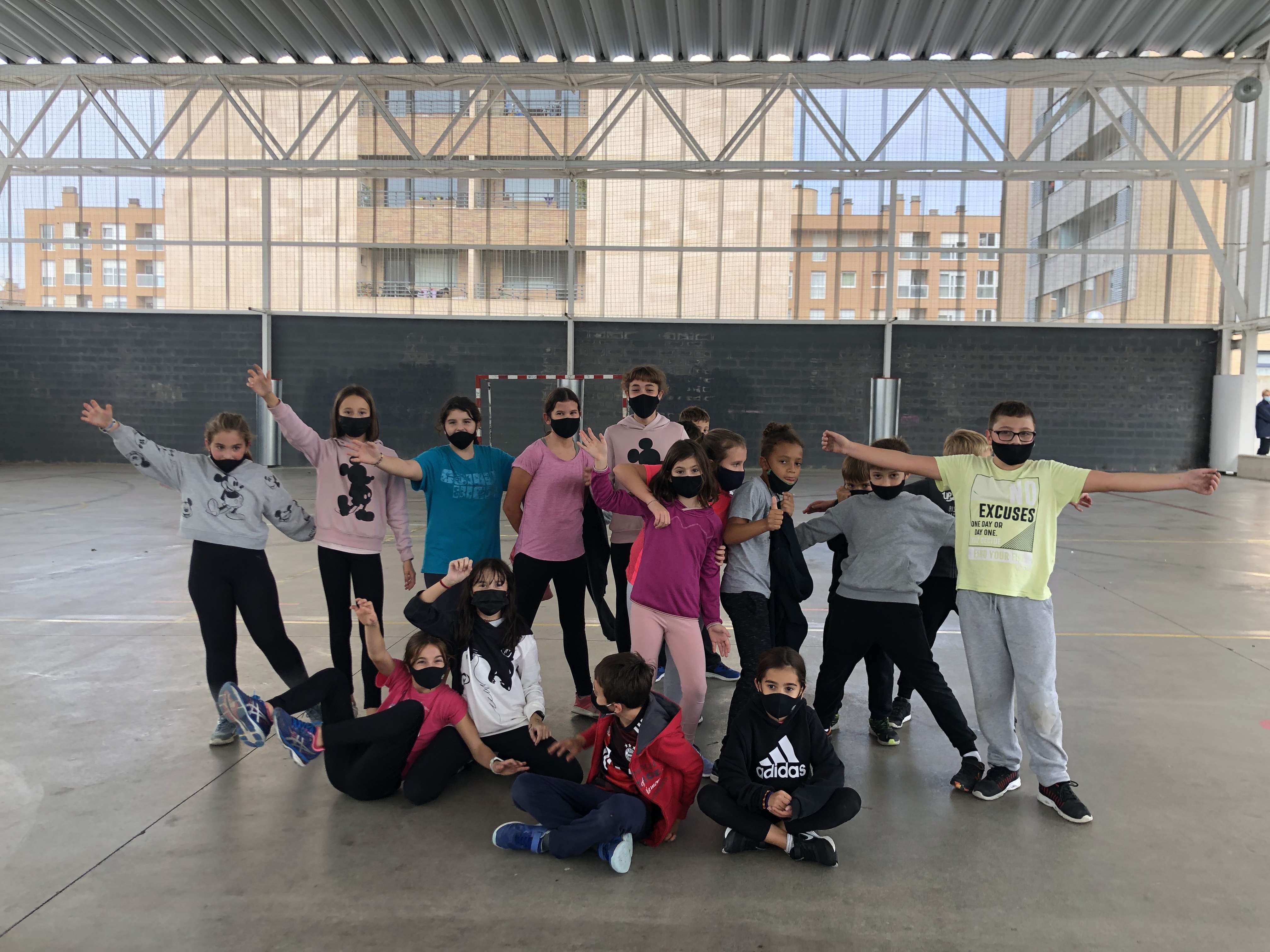 Grupo de niños y niñas en una pista deportiva cubierta, posando en grupo con gestos divertidos y brazos en alto.