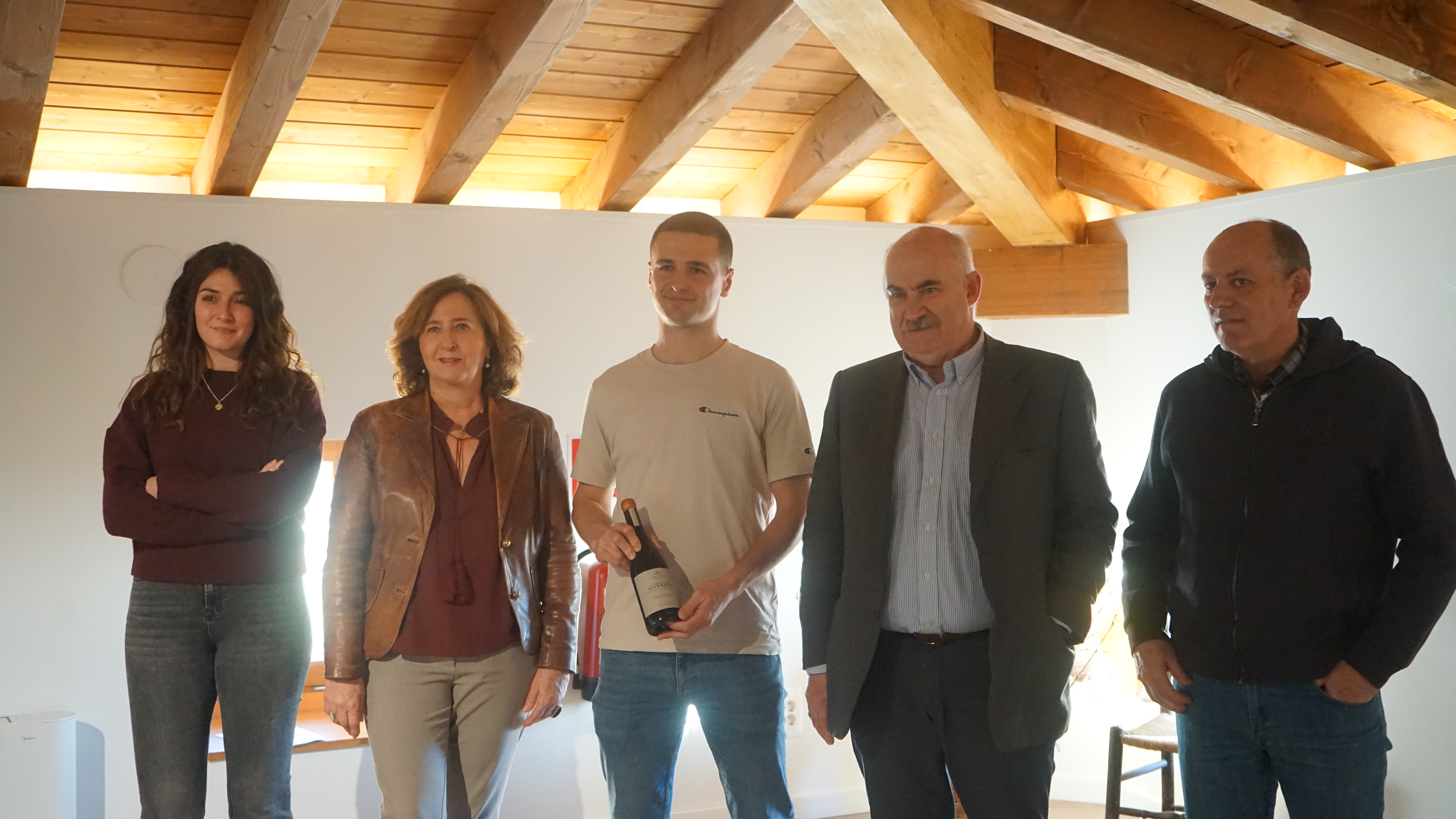 4 personas posando junto con una botella de vino