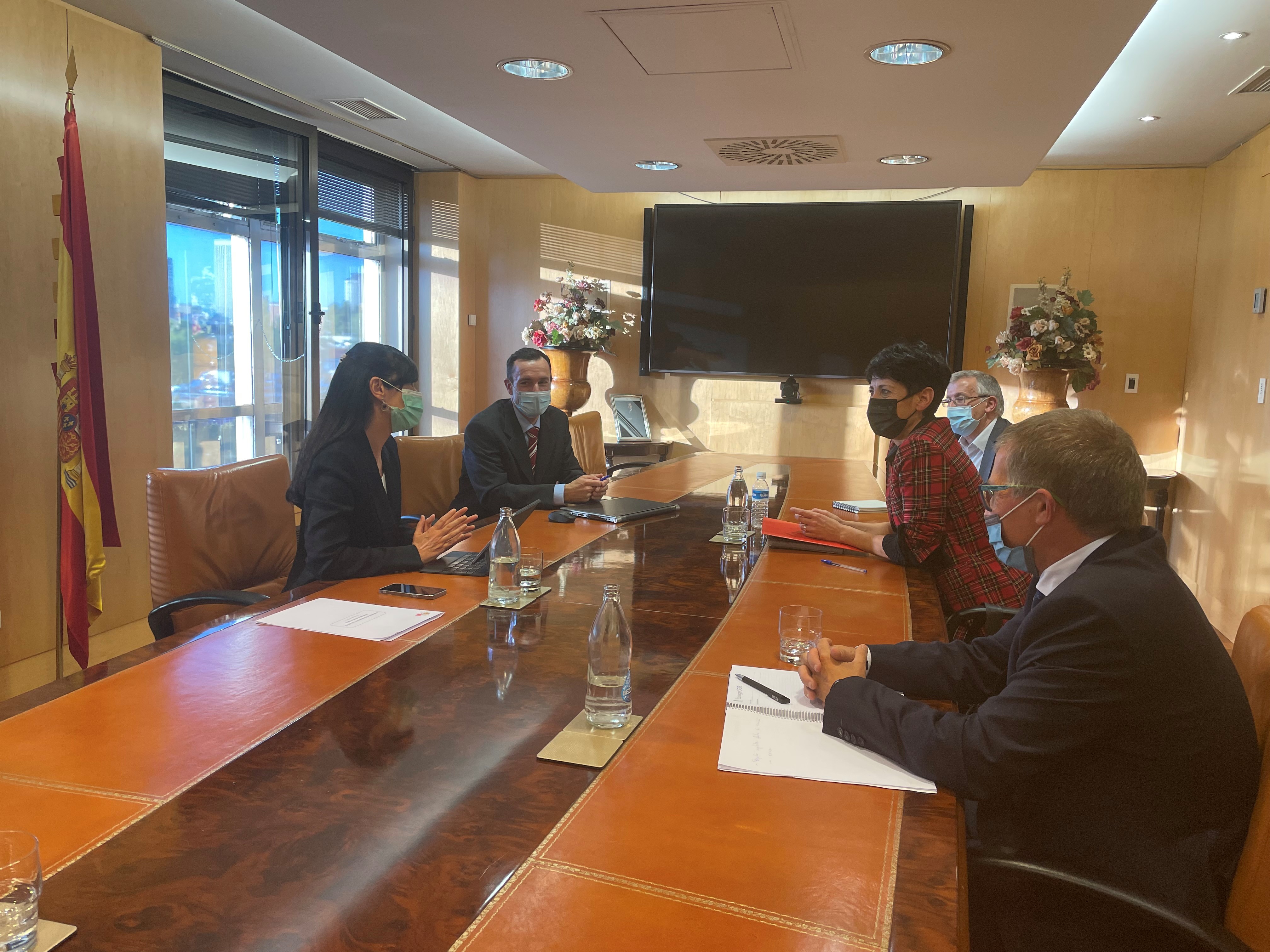 Fotografía de una mesa alargada de reuniones. Se ve a ambos lados a las 5 personas asistentes a la reunión, 2 a mano izquierda y 3 a mano derecha.