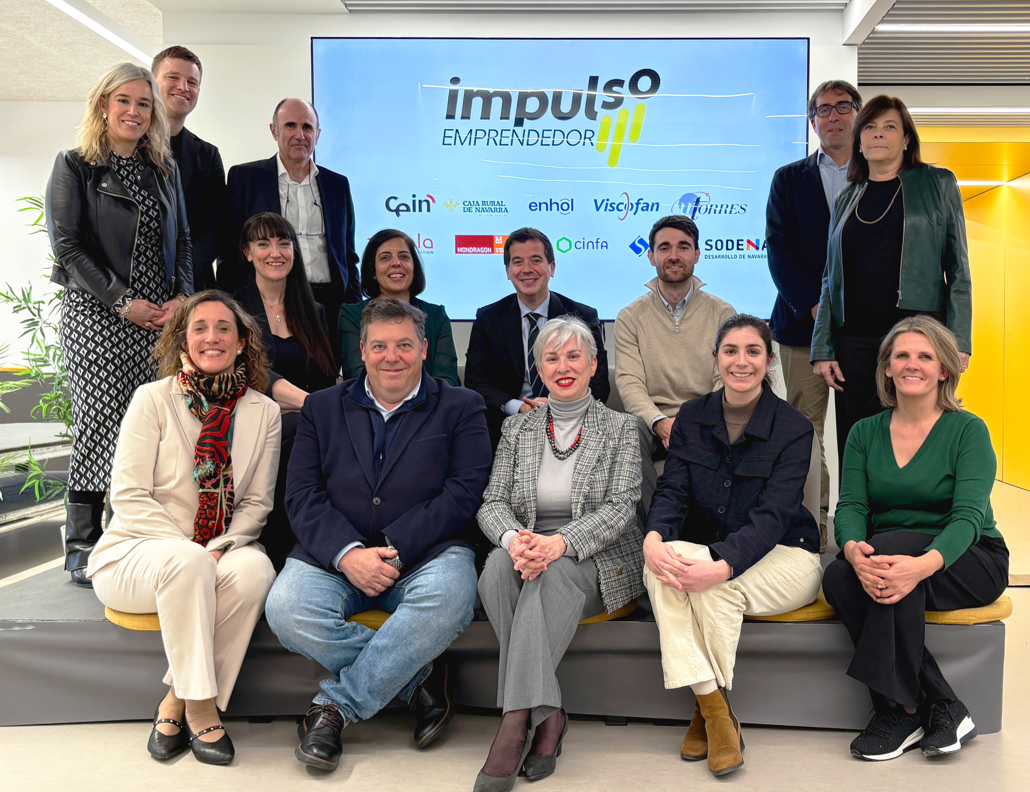 Foto grupal de varias personas sentadas y de pie delante del logo de la iniciativa