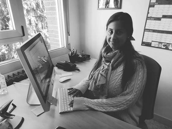 Fotografía en blanco y negro de Marina Muñoz, sentada delante del ordenador, sonriente y mirando a cámara.