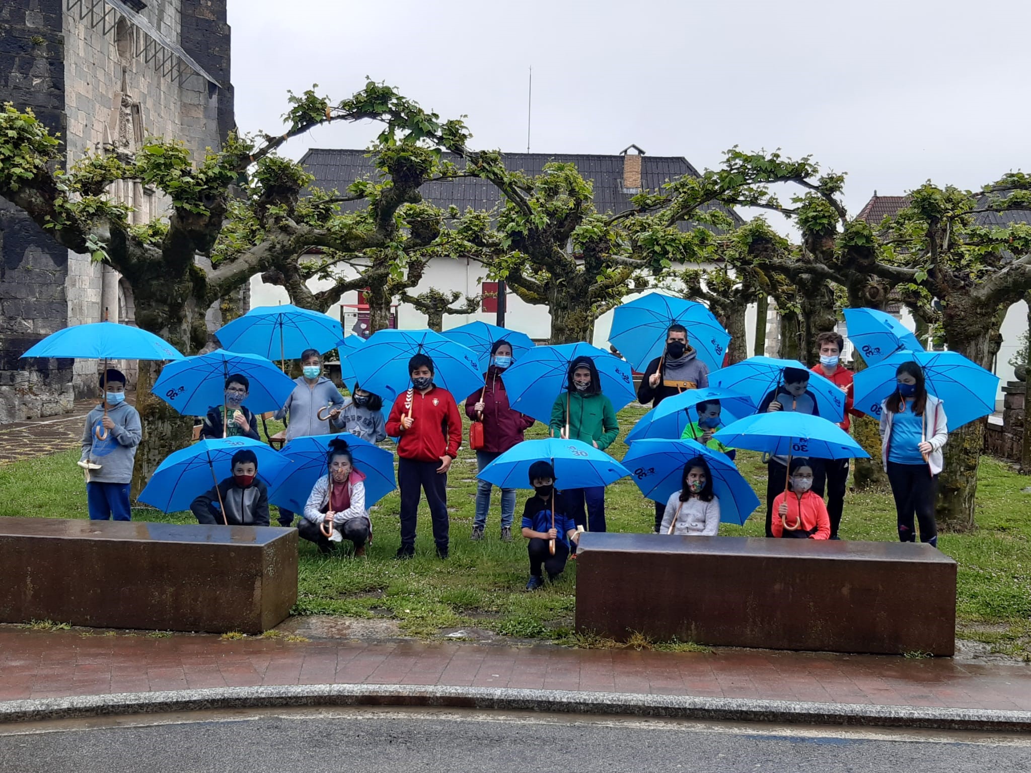 Fotografía de diecisiete niños y niñas con paraguas azules en un parque