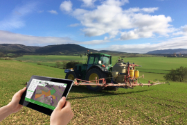 Plataforma AGROasesor abierta en una tablet con un tractor de fondo