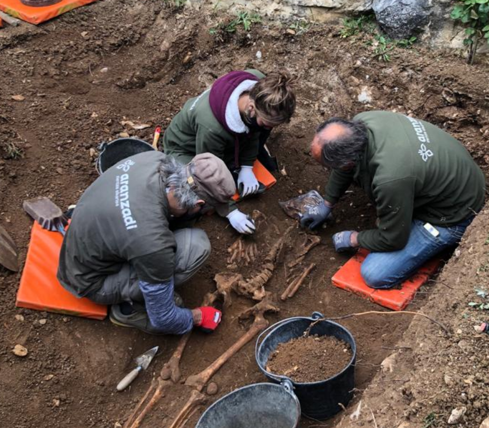 Fotografía de tres personas exhumando los restos en una franja de tierra.