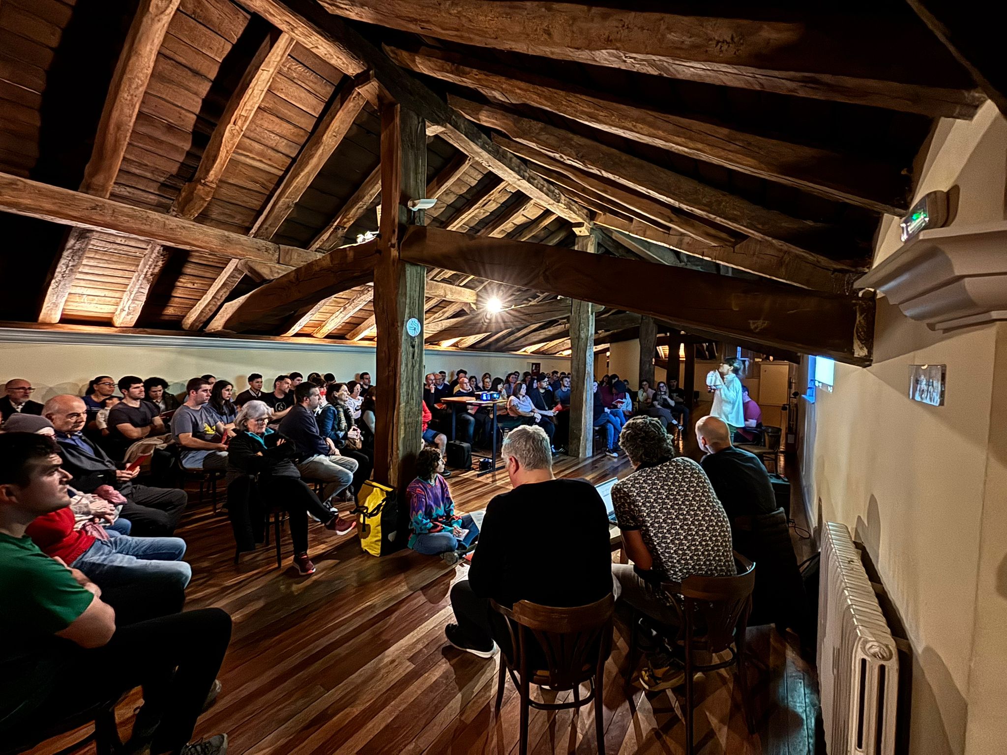 Fotografía de un grupo de gente en una boardilla sentados escuchando