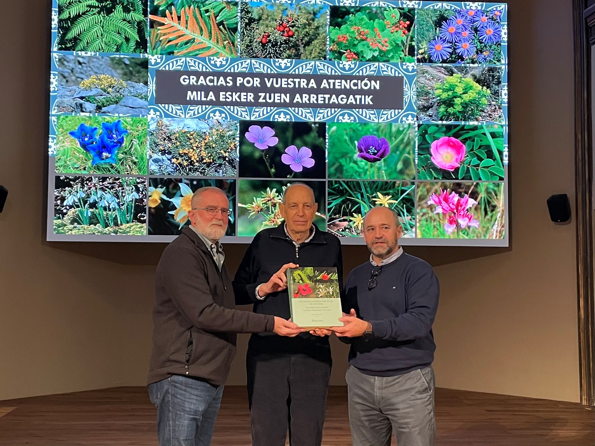 Fotografía donde se ve a tres hombres mirando a cámara y sosteniendo conjuntamente un ejemplar del atlas presentado