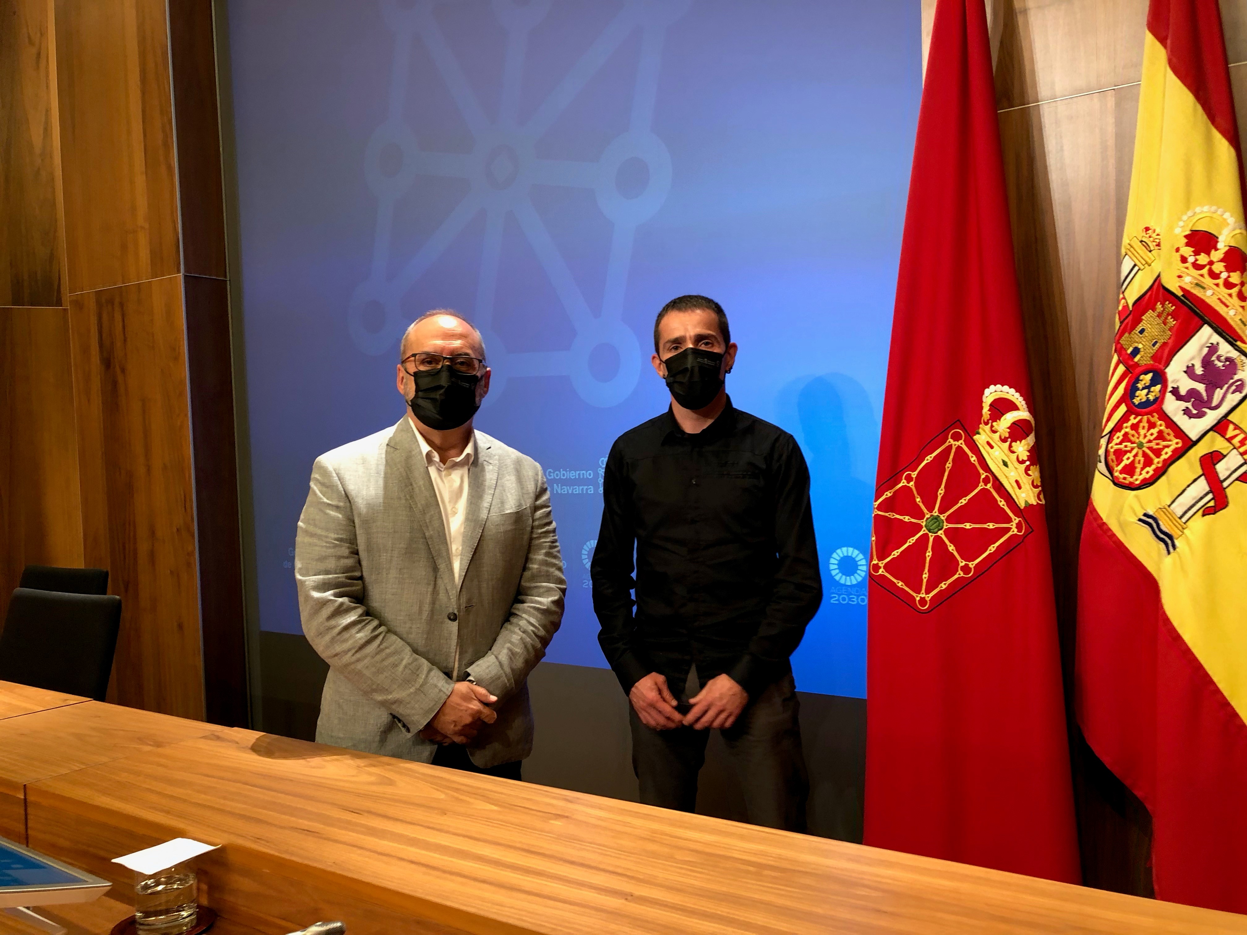 Fotografía interior de dos hombres de pie con las banderas de España y Navarra detrás de ellos