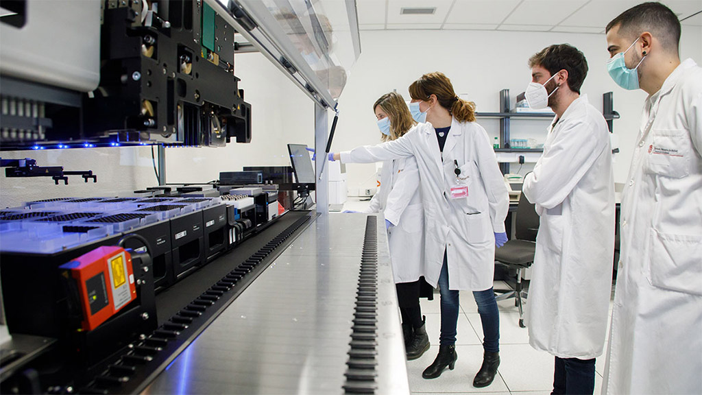 Fotografía interior de un laboratorio con cuatro personas con batas blancas. 