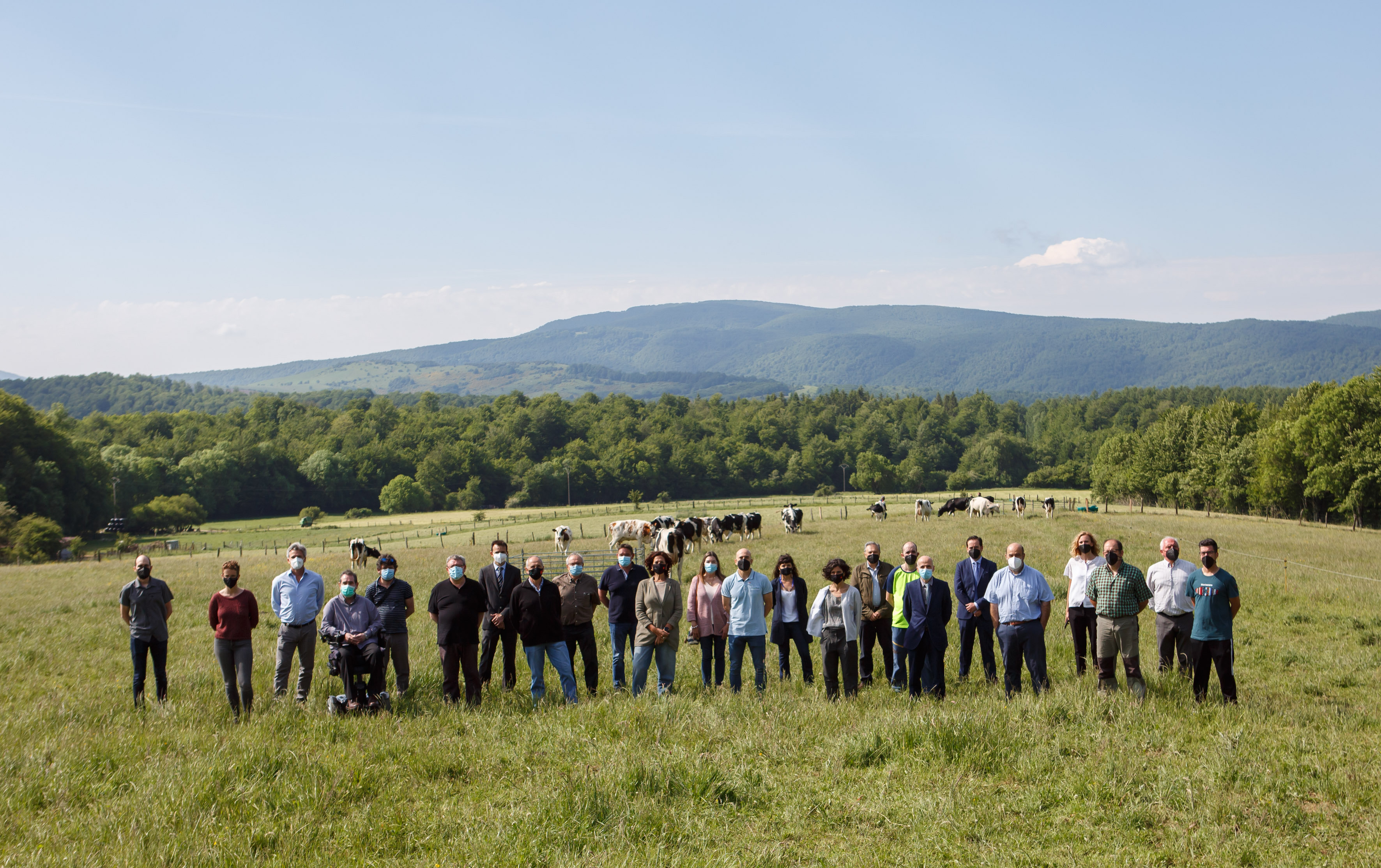 Fotografía de varias personas de pie en un campo con vacas detrás