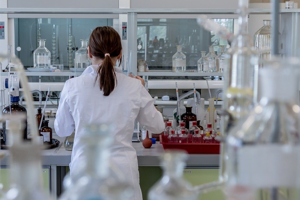 Fotografía de una mujer de espaldas en un laboratorio con tubos de ensayo y material de laboratorio
