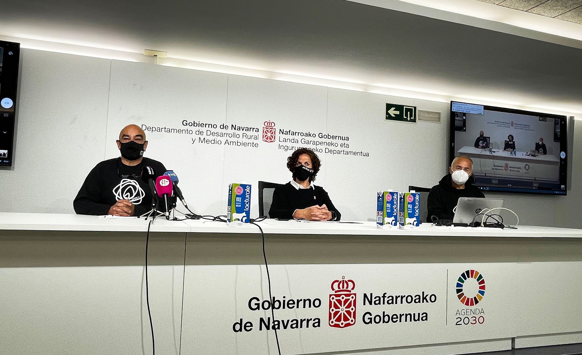 Fotografía de dos hombres y una mujer sentados en una mesa blanca. 