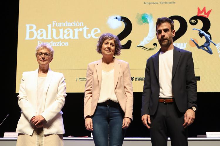 Fotografía de tres personas de pie y detrás el cartel promocional de la programación