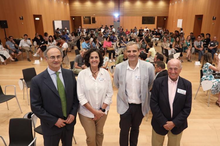 Fotografía de cuatro personas de pie dentro de una sala y otras sentadas.