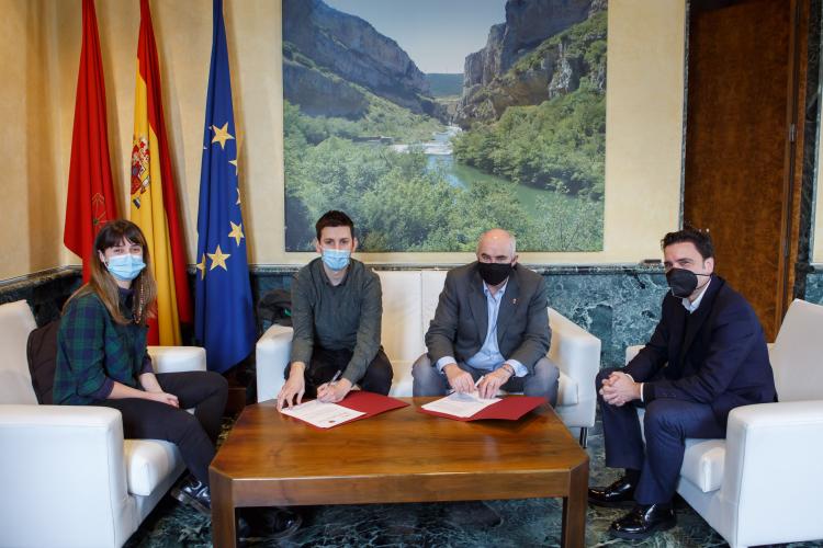 Fotografía de tres hombres y una mujer sentados en un sofá en un despacho firmando.