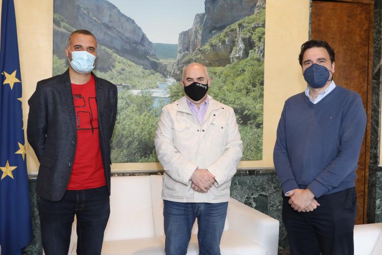 Fotografía de interior con tres hombres de pie delante de un cuadro con un paisaje natural