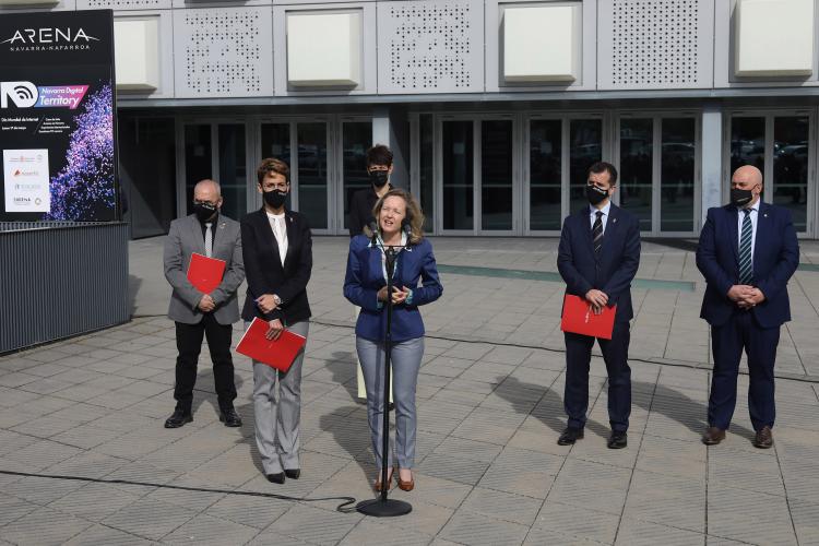 Fotografía exterior de tres mujeres y tres hombres de pie, una de las mujeres hablando con un micrófóno de pie.