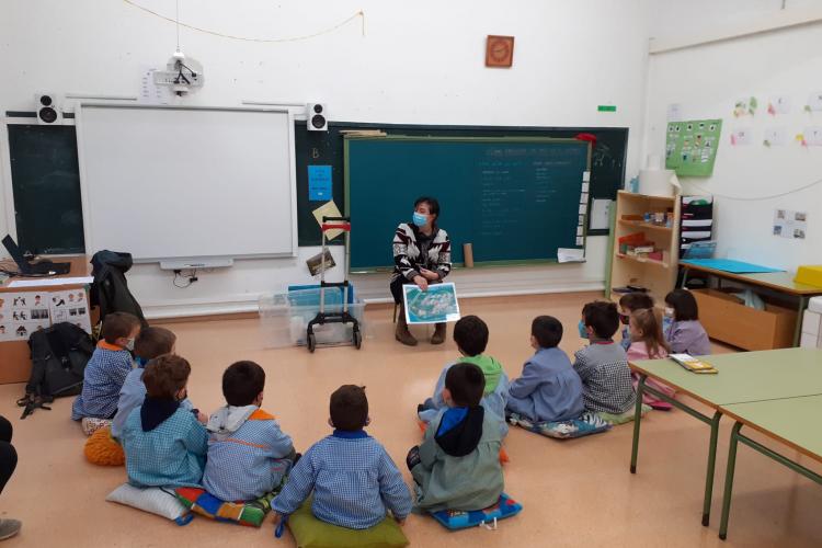Fotografía de doce niños sentados en el suelo en un aula y una persona trabajadora de Nilsa