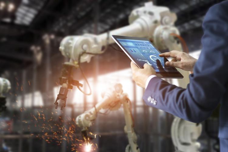 Dos brazos sujetando una tablet y detrás maquinaria de construcción.