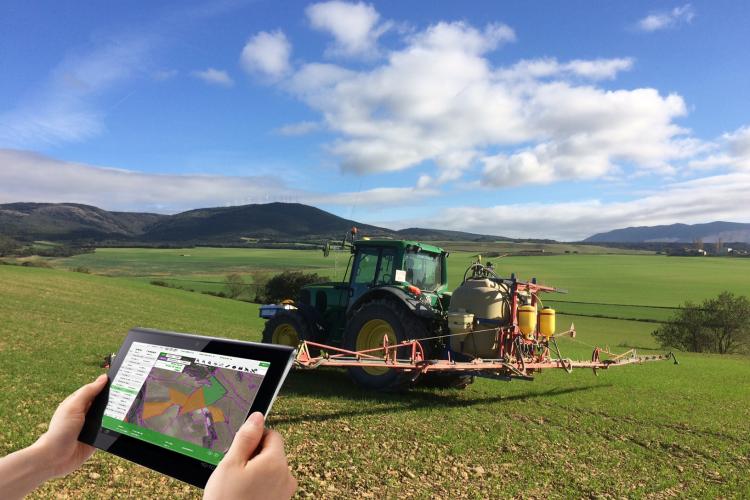 Fotografía de un tractor en el campo y una mano sosteniendo una tablet