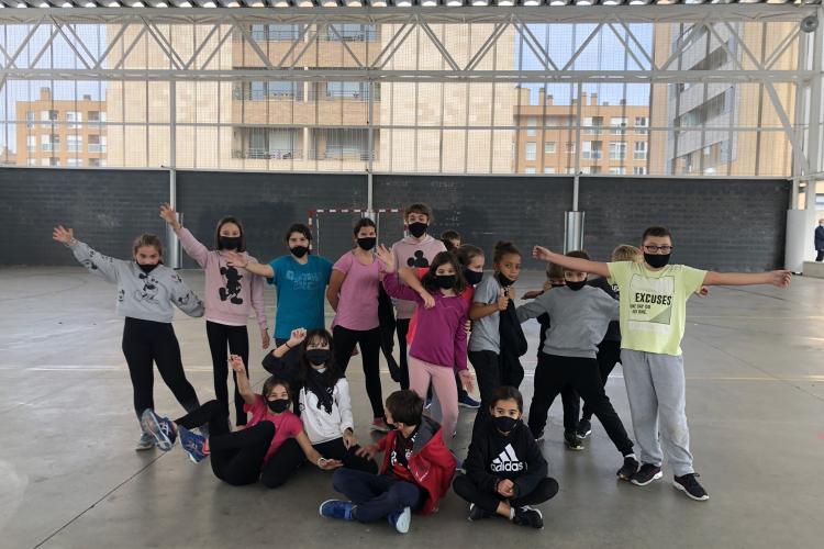 Grupo de niños y niñas en una pista deportiva cubierta, posando en grupo con gestos divertidos y brazos en alto.