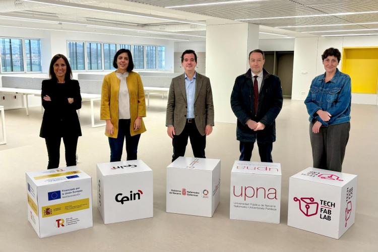 Fotografía de 5 personas mirando a cámara, de pie, en medio de una sala de oficinas de fondo. 