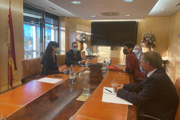 Fotografía de una mesa alargada de reuniones. Se ve a ambos lados a las 5 personas asistentes a la reunión, 2 a mano izquierda y 3 a mano derecha.