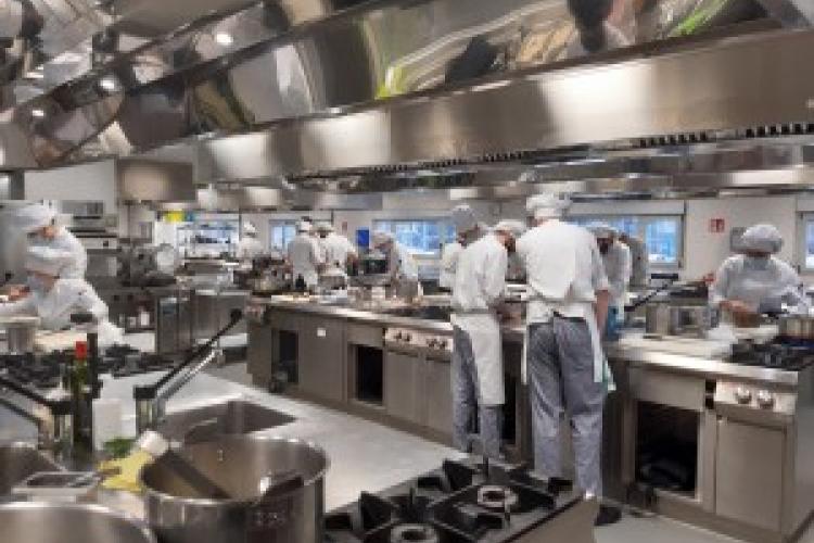 Fotografía de una cocina industrial y varios cocineros cocinando