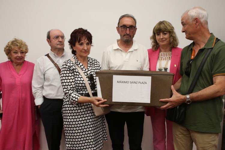 Fotografía de varias personas de pie y cuatro de ellas sujetando una caja de madera