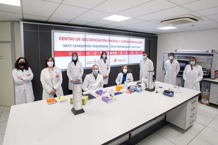 Fotografía de un laboratorio donde aparecen seis mujeres y tres hombres con batas blancas alrededor de una mesa. 