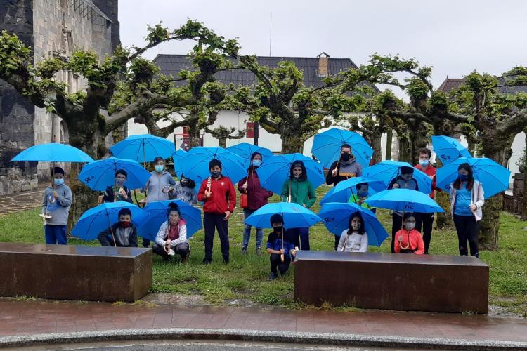 Fotografía de diecisiete niños y niñas con paraguas azules en un parque