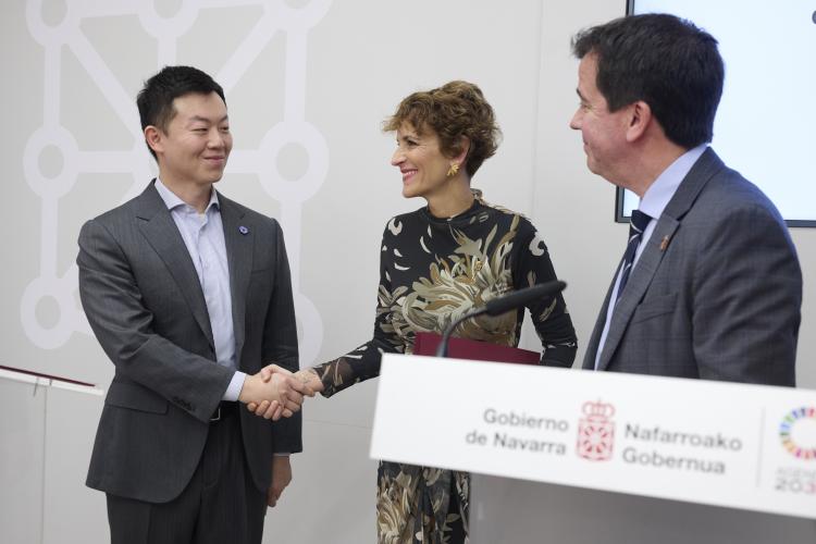 Tres personas delante de un atril. Dos de ellas se estrechan la mano sonrientes mientras el tercero les mira