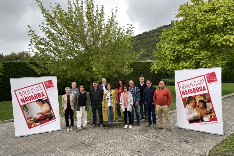 Fotografía de exterior de varias personas de pie y en cada lado el cartel promocional 