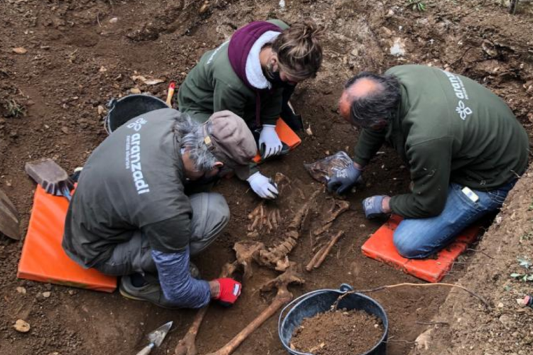 Fotografía de tres personas exhumando los restos en una franja de tierra.