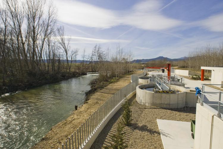 Fotografía exterior donde se ve un río, árboles y una depuradora.