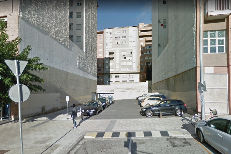 Fotografía exterior donde aparecen tres edificios y una calle con coches aparcados