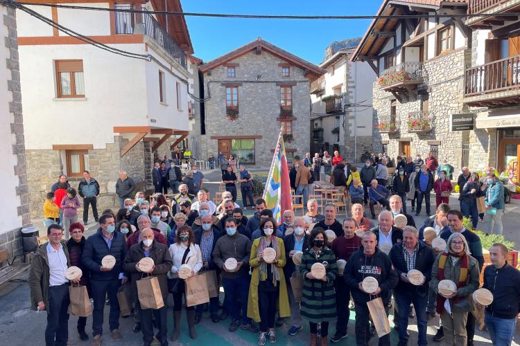 Fotografía exterior donde varias personas están de pie en una plaza con un queso del Roncal en sus manos.