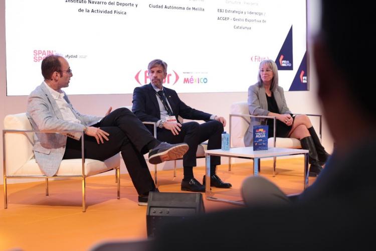 Aparecen 3 personas sentadas hablando en un escenario