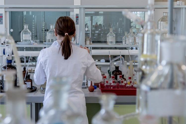 Fotografía de una mujer de espaldas en un laboratorio con tubos de ensayo y material de laboratorio