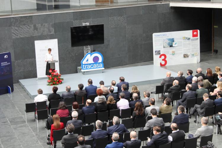 En la imagen, tomada desde un nivel superior, se ve a la presidenta de Navarra en un pequeño escenario, hablando desde una atril, y todo un patio de butacas con personas mirando al frente (de espaldas a la fotografía).