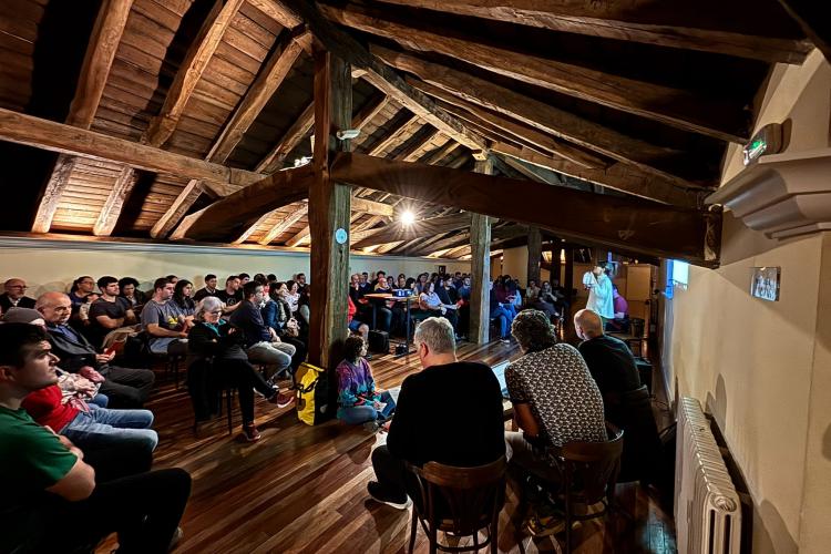 Fotografía de un grupo de gente en una boardilla sentados escuchando