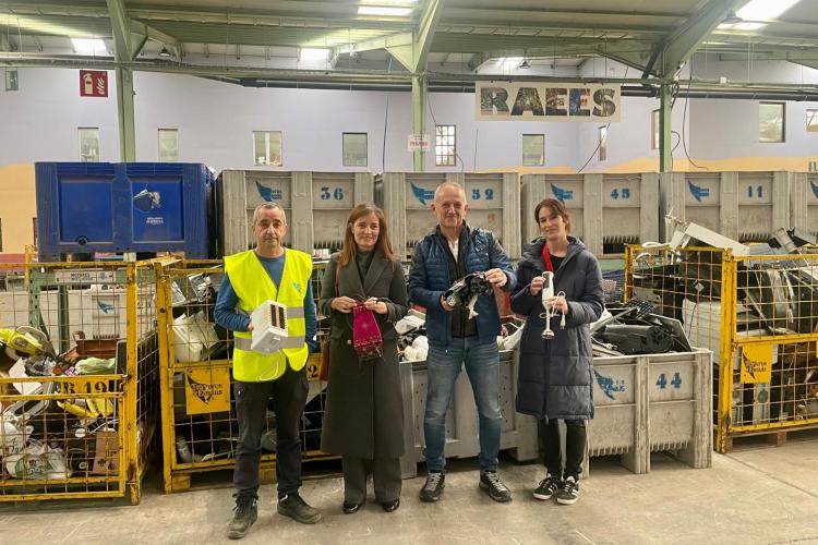 Fotografía de cuatro personas, dos hombres y dos mujeres, de cuerpo entero mostrando aparatos reciclados a cámara